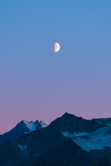 Alaskan mountains with half moon and pink skies after sunset during blue hour