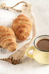 Crispy croissant and cup of coffee on a wooden table