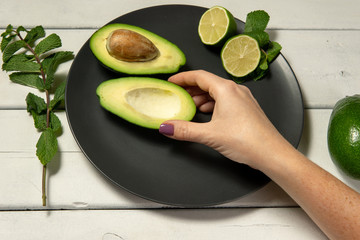 Woman preparing raw avocado and lime on a white wooden backgroung