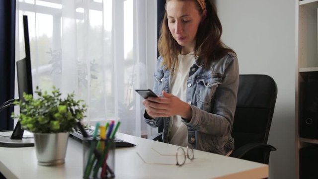 Happy smiling woman receiving nice message and typing sms on her smartphone. Woman working at her home office, freelace working