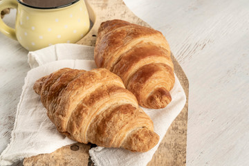Crispy croissant and cup of coffee on a wooden table