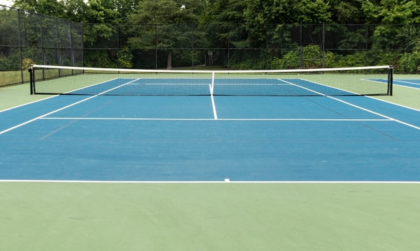 Blue Outdoor Tennis Court With Green Boarder And Trees In Background