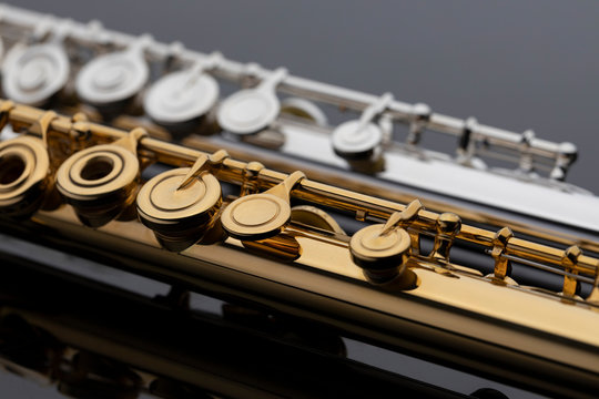 Two shiny gold and silver plated flutes on a reflective surface. An instrument common in a symphony orchestra