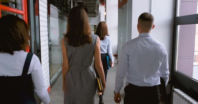 colleagues go down the corridor of the office to the exit. people company employees and businessmen walk together along the corridor of the office. four people walking in slow motion. people walk away