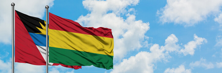 Antigua and Barbuda with Bolivia flag waving in the wind against white cloudy blue sky together. Diplomacy concept, international relations.