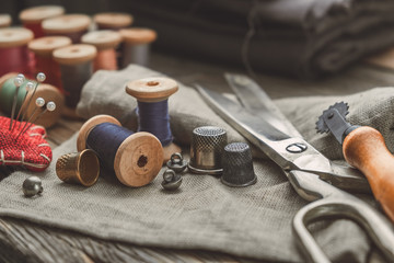 Retro sewing items: tailoring scissors, cutting knife, thimble, wooden thread spools, cushion for including pins, fabrics and sewing accessories. - Powered by Adobe
