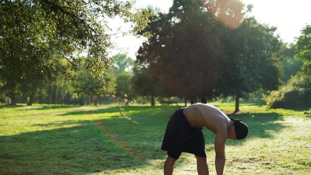 Sexy muscular build man showing morning workout in the park. Naked professional coach doing exercises for stretching muscles. Young sportsman training outdoors, sport motivation and final result
