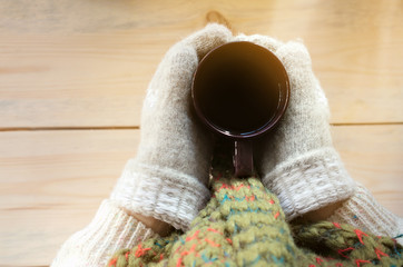 mug with a hot drink in the hands of a young girl dressed in knitted mittens, warm winter scarf