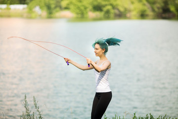 portrait of a beautiful young woman with green hair in a park near a lake with a skipping rope