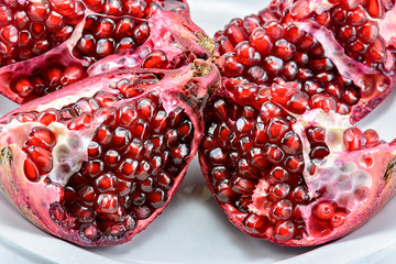 peeled pomegranate seeds in a cup along with a fraction of fresh pomegranate isolated on white background