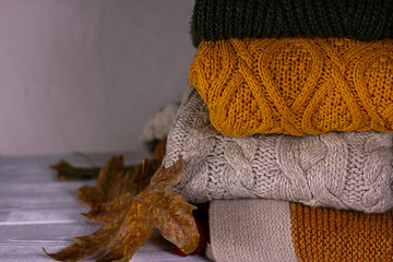 Fototapeta na wymiar Stack of warm woolen colorful knitted winter and autumn sweaters with dray leaves autumn background close up image.