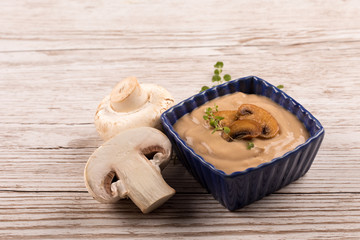 mushroom soup in blue bowl with roasted mushrooms and herbs on wooden table