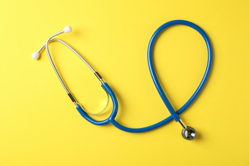 Stethoscope on yellow background, top view and space for text