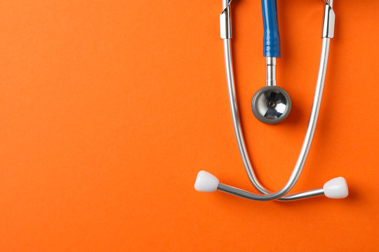 Stethoscope on orange background, space for text. Healthcare
