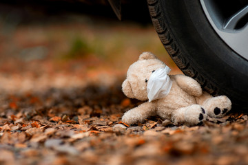 teddy bear in a medical mask crushed by a car
