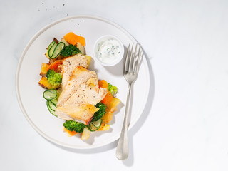 Healthy dinner or lunch with chicken, grilled potatoes, cucumber, carrot, broccoli, yogurt sauce dressing, light background, copyspace. Proper nutrition. Dietary menu. Flat lay. Top view. Hard light.