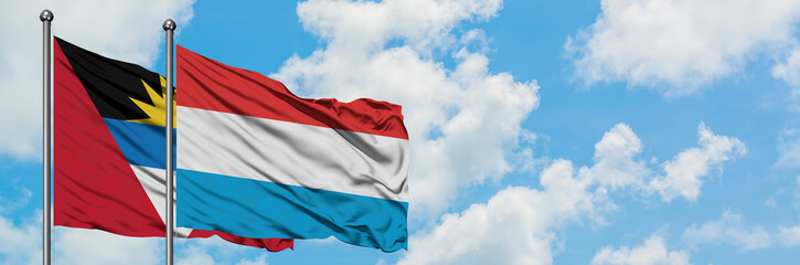 Antigua and Barbuda with Luxembourg flag waving in the wind against white cloudy blue sky together. Diplomacy concept, international relations.