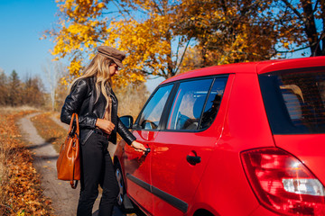 Opening car door. Woman opens red car with key on autumn road