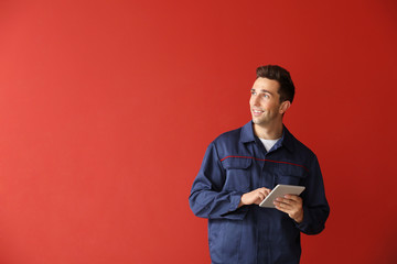 Male car mechanic with tablet computer on color background