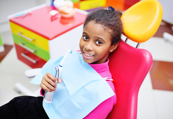 cute black baby girl smiling sitting in a red dental chair