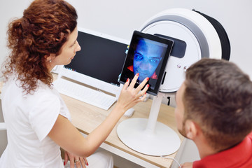 facial skin diagnostics equipment for dermatology and cosmetology. A cosmetologist analyzes the...