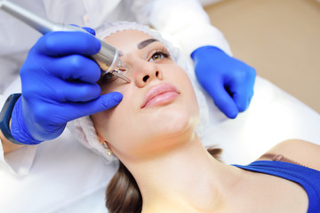 Obraz na płótnie Canvas the surgeon beautician removes pigmentation and vascular nets on the skin of the patient-a beautiful young woman neodymium laser. Laser cosmetology