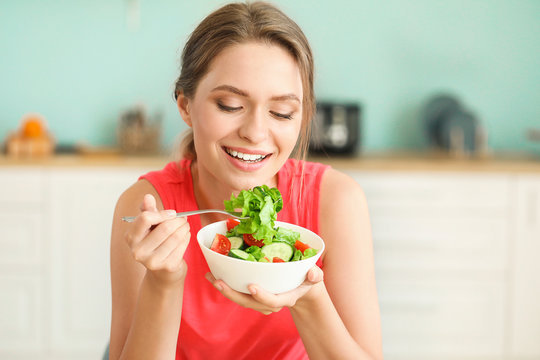 Young woman eating healthy vegetable salad in kitchen. Diet concept