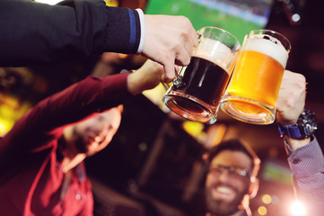 a group of young men's friends in a bar or pub drinking beer with glasses and watching football during the celebration of Oktoberfest