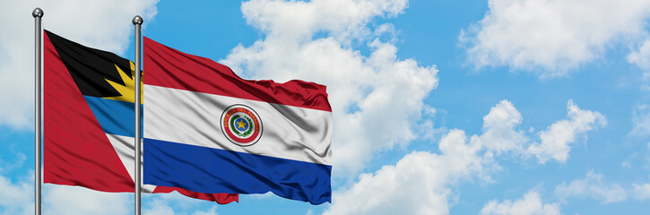 Antigua and Barbuda with Paraguay flag waving in the wind against white cloudy blue sky together. Diplomacy concept, international relations.