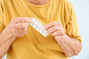 Elderly woman with pills on light background, closeup