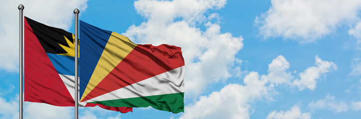 Antigua and Barbuda with Seychelles flag waving in the wind against white cloudy blue sky together. Diplomacy concept, international relations.