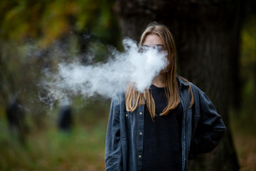 Vape teenager. Young beautiful white teenage girl in glasses and casual clothes vaping electronic...