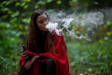 Vape teenager. Young beautiful white teenage girl in casual clothes vaping electronic cigarette on the street in the dark forest in the autumn evening. Bad habit. Vaping activity.