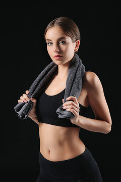 Sporty young woman with towel against dark background