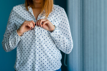 Close up on midsection of young women girl button or unbutton white shirt with spots in front of the blue wall at home alone changing clothes dressing or undressing hands