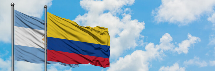 Fototapeta premium Argentina and Colombia flag waving in the wind against white cloudy blue sky together. Diplomacy concept, international relations.