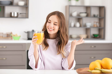 Beautiful young woman drinking orange juice in kitchen