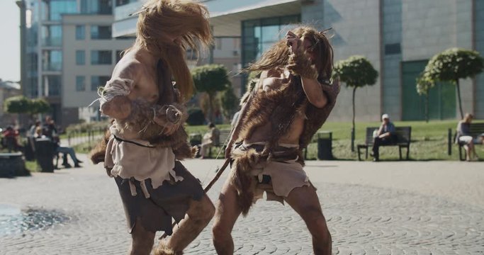 In modern city neanderthals man of hunter-gatherers in animal fur holding prehistoric weapon dancing hunting animals look around wonder timetraveler evolution caveman civilization slow motion