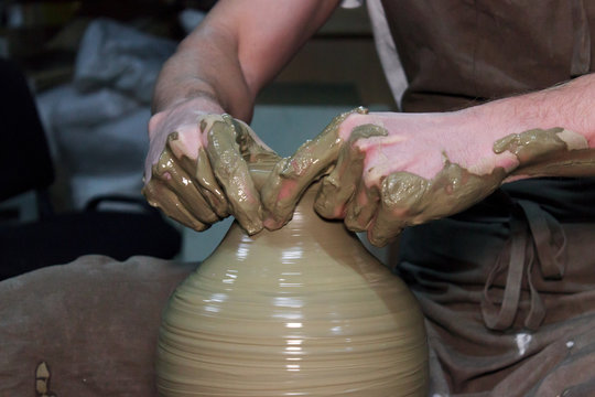 experienced potter makes a large vase on a potter's wheel. twisting a narrow neck. clay product.