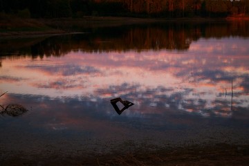 Wood pallet stuck in still lake during sunset, with reflection of sky in lake.