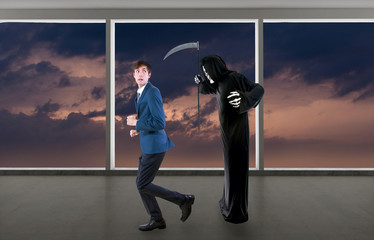 Man in a Halloween grim reaper ghost costume chasing, mocking and making fun of scared businessman...