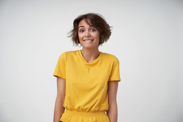 Beautiful young brunette woman with short haircut feeling shy and biting her underlip while looking...