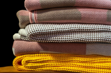 A stack of knitted colored blankets on wooden shelf, black isolated