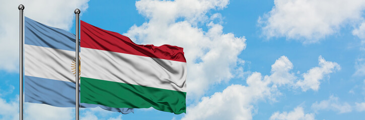 Obraz premium Argentina and Hungary flag waving in the wind against white cloudy blue sky together. Diplomacy concept, international relations.