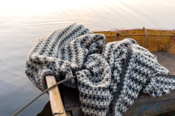 Striped knitted wool warm blanket in a boat on lake water, sunset light