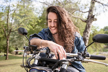 Fototapeta na wymiar Joven motociclista sonriente de pelo largo en el parque 