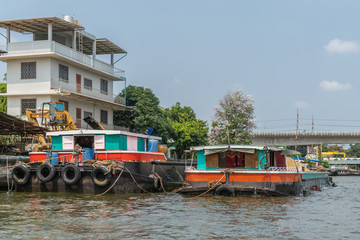 Fototapeta na wymiar Bangkok city, Thailand - March 17, 2019: Bangkok Noi Canal. Two Big freighter barges with colored cabin and housing on top docked along the canal under blue sky. White building in back. Charan Sanitw