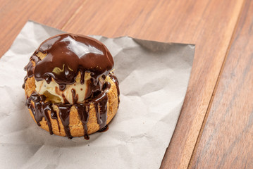 Profiteroles with ice cream and chocolate. Eclairs with black chocolate on wooden background. Traditional French dessert.