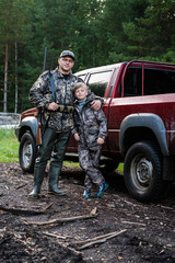 Father and son came to the forest for hunting together. Standing with a shotgun rifle in front of pickup truck.
