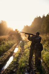 Rifle Hunter and His Son Silhouetted in Beautiful Sunset. Huntsman with a boy and rifle in a forest on a sunrise. - 297435113